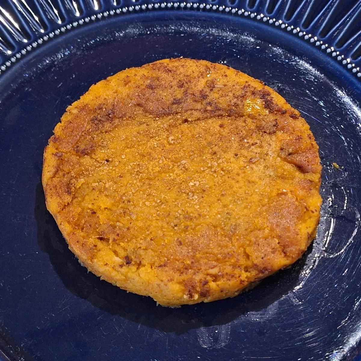 Burger di zucca cotto in padella, con doratura non uniforme in superficie.